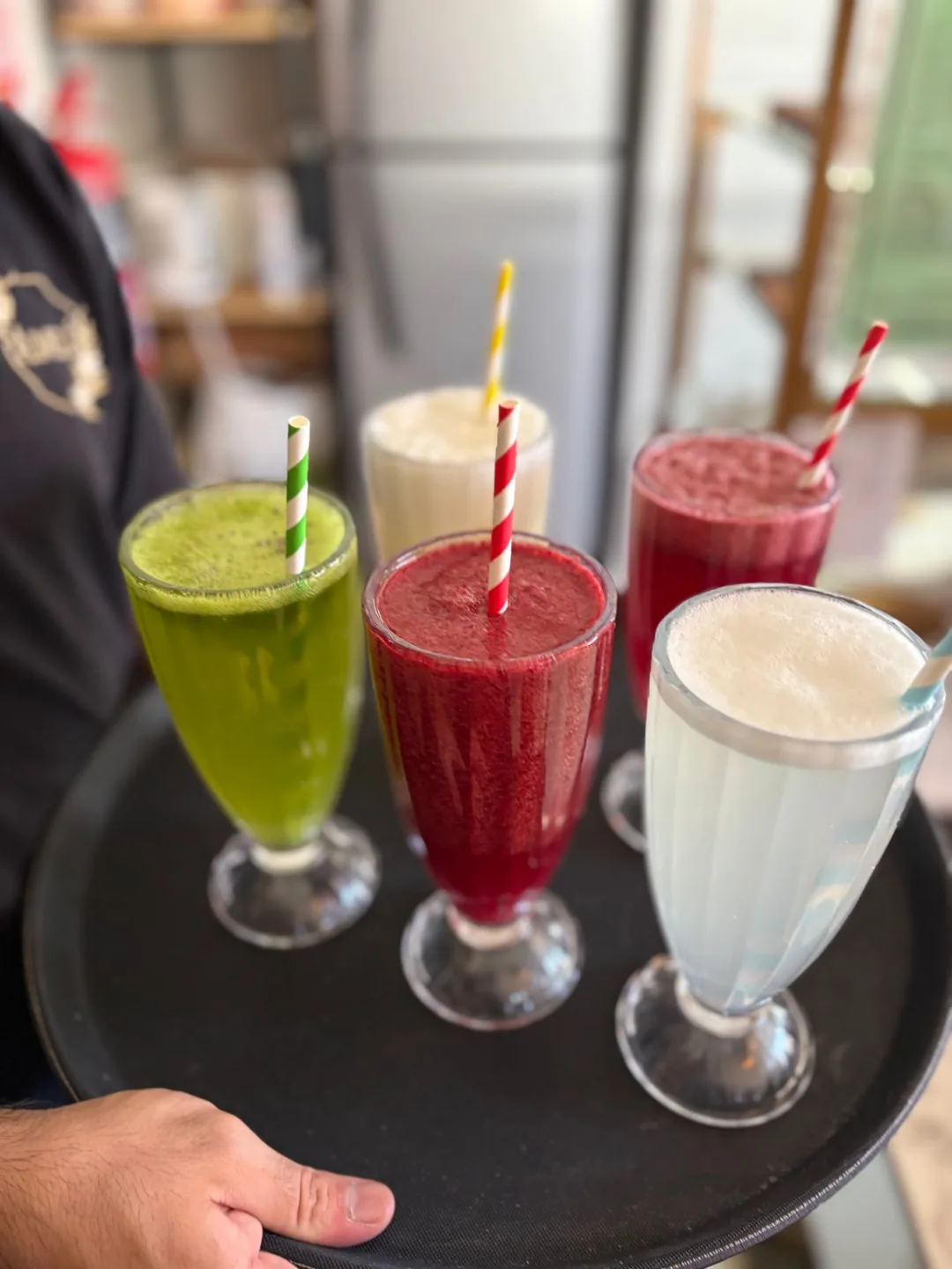 Bandeja con licuados de kiwi, frutos rojos, banana y otro sabor claro, servidos en copas altas